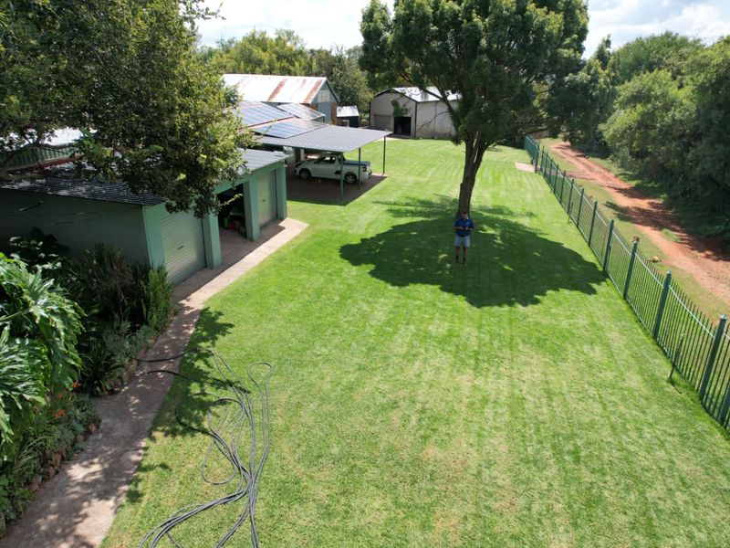Aerial view of the farm property featuring a large lawn, garage block with solar panels, carport, and secure perimeter fencing.
