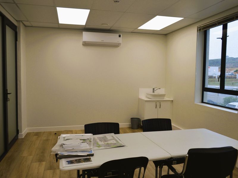 A clean, functional office space featuring a built-in vanity with sink, split-system air conditioning, recessed lighting, and wood-look laminate flooring.