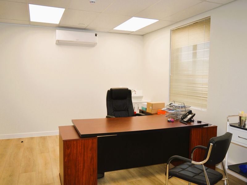 A clean, professional office space featuring wood-look laminate flooring, recessed ceiling lighting, and a wall-mounted split-system air conditioner.