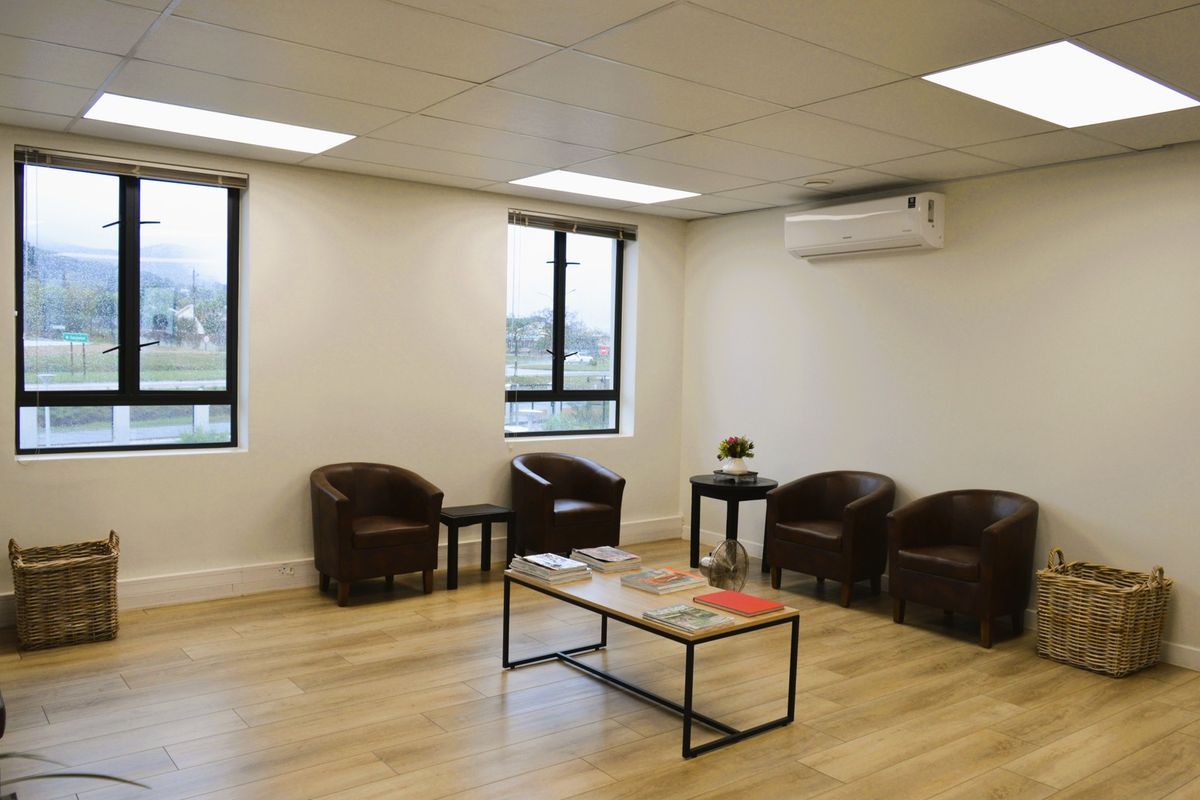 A bright and professional office space featuring wood-look laminate flooring, recessed ceiling lighting, and a wall-mounted air conditioning unit.