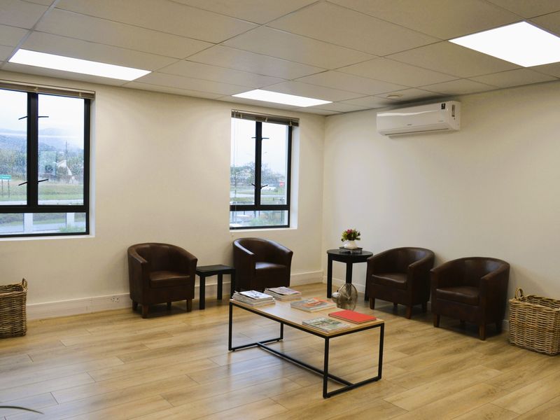 A bright and professional office space featuring wood-look laminate flooring, recessed ceiling lighting, and a wall-mounted air conditioning unit.