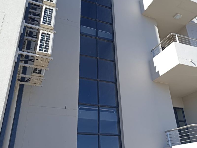 Exterior view of a modern commercial building facade featuring a full-height glass window section, multiple external air conditioning units, and tiered balconies.