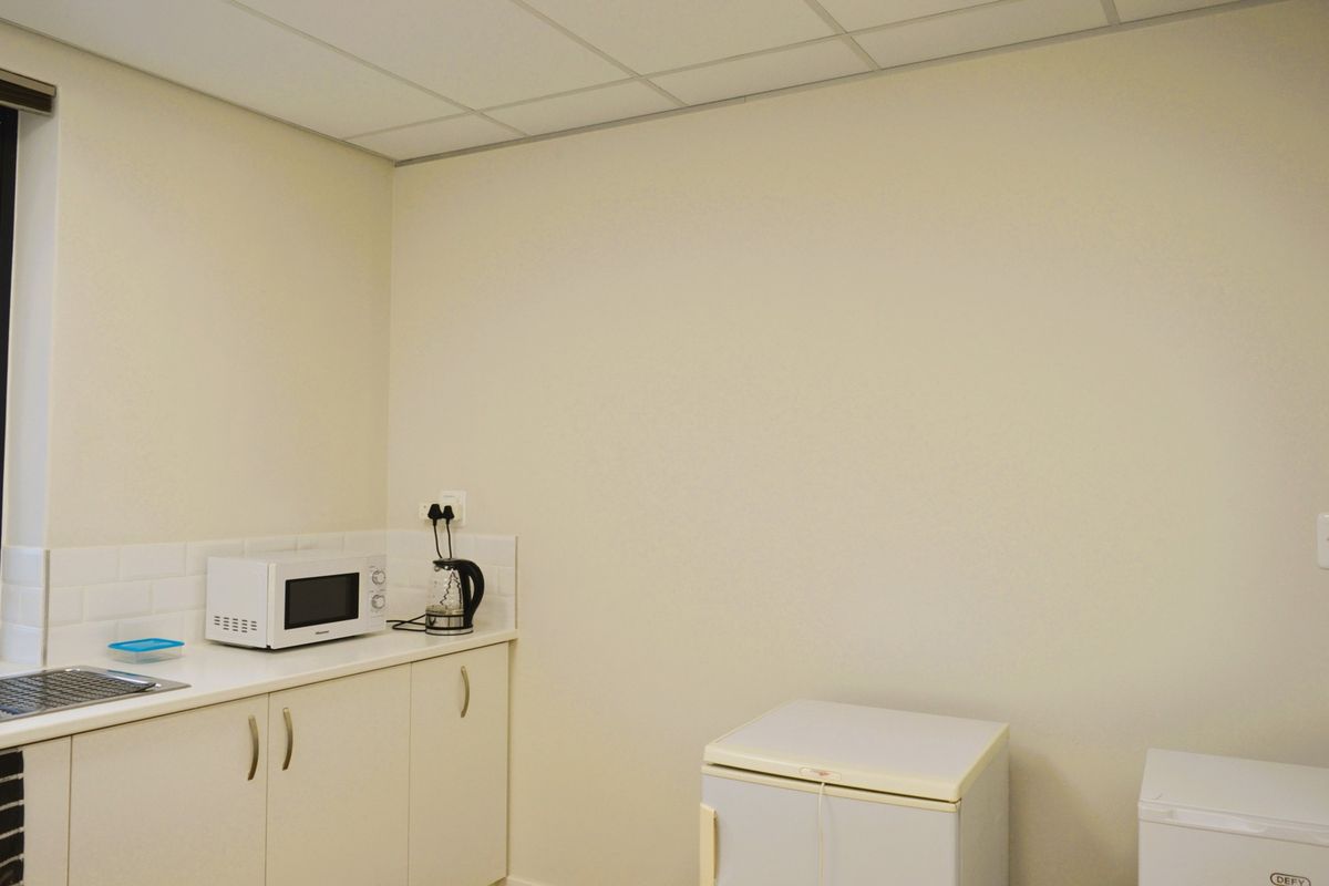 A functional commercial kitchenette featuring built-in cabinetry, a stainless steel sink, tiled splashback, and a suspended ceiling.