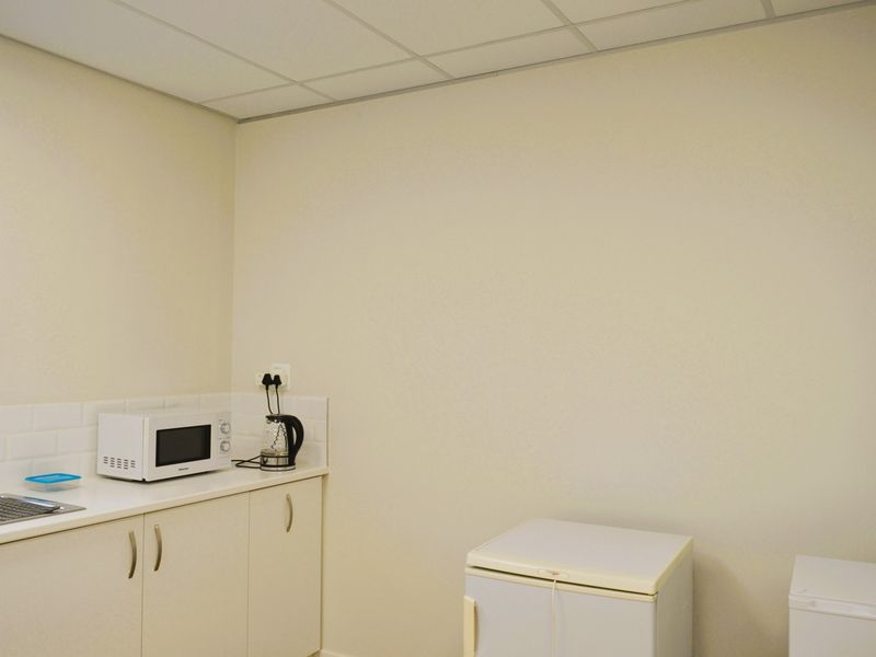 A functional commercial kitchenette featuring built-in cabinetry, a stainless steel sink, tiled splashback, and a suspended ceiling.