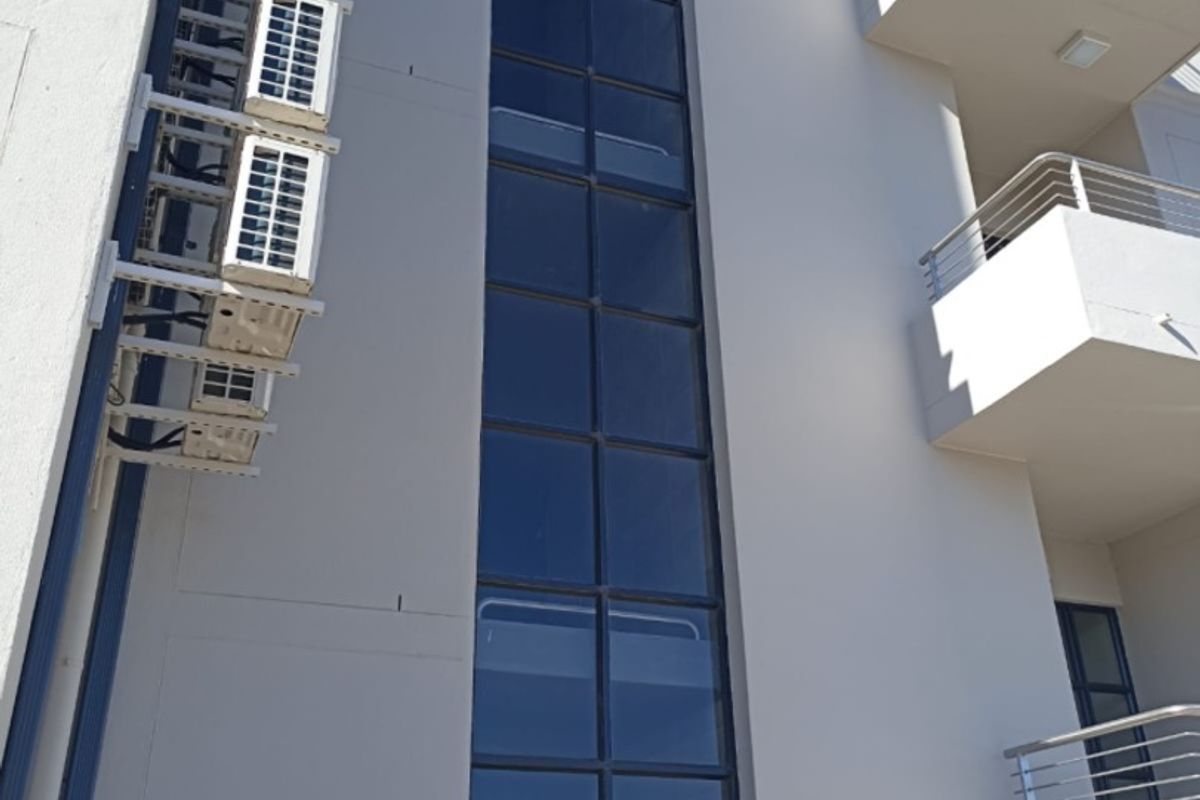 A view of the building's rear facade featuring a tall glass curtain wall, multiple external air conditioning units, and balconies with modern metal railings.