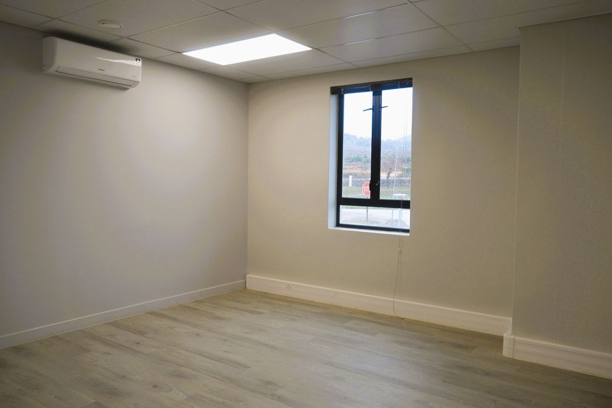 A clean, empty office space featuring modern laminate flooring, a drop ceiling with recessed lighting, and a wall-mounted split-system air conditioning unit.