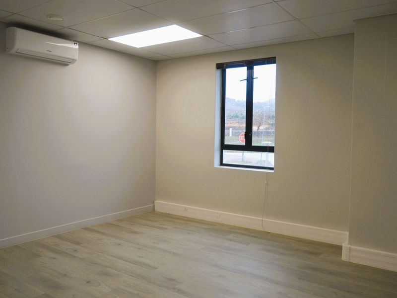 A clean, empty office space featuring modern laminate flooring, a drop ceiling with recessed lighting, and a wall-mounted split-system air conditioning unit.