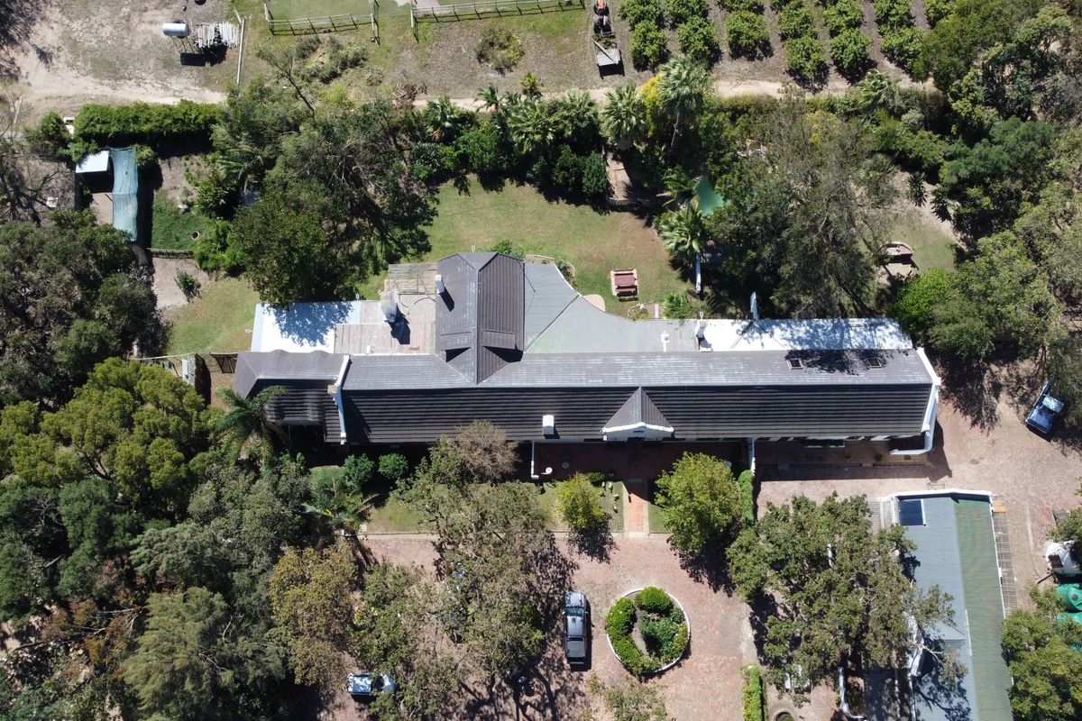 Aerial view of a farm property featuring a large main residence with a tiled roof, surrounded by mature trees, landscaped gardens, and paved driveway.