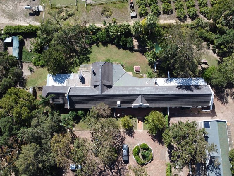 Aerial view of a farm property featuring a large main residence with a tiled roof, surrounded by mature trees, landscaped gardens, and paved driveway.