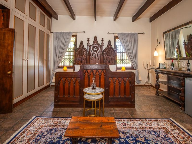 A well-maintained bedroom featuring exposed timber ceiling beams, tiled flooring, and custom built-in cabinetry, complemented by decorative leaded glass windows.