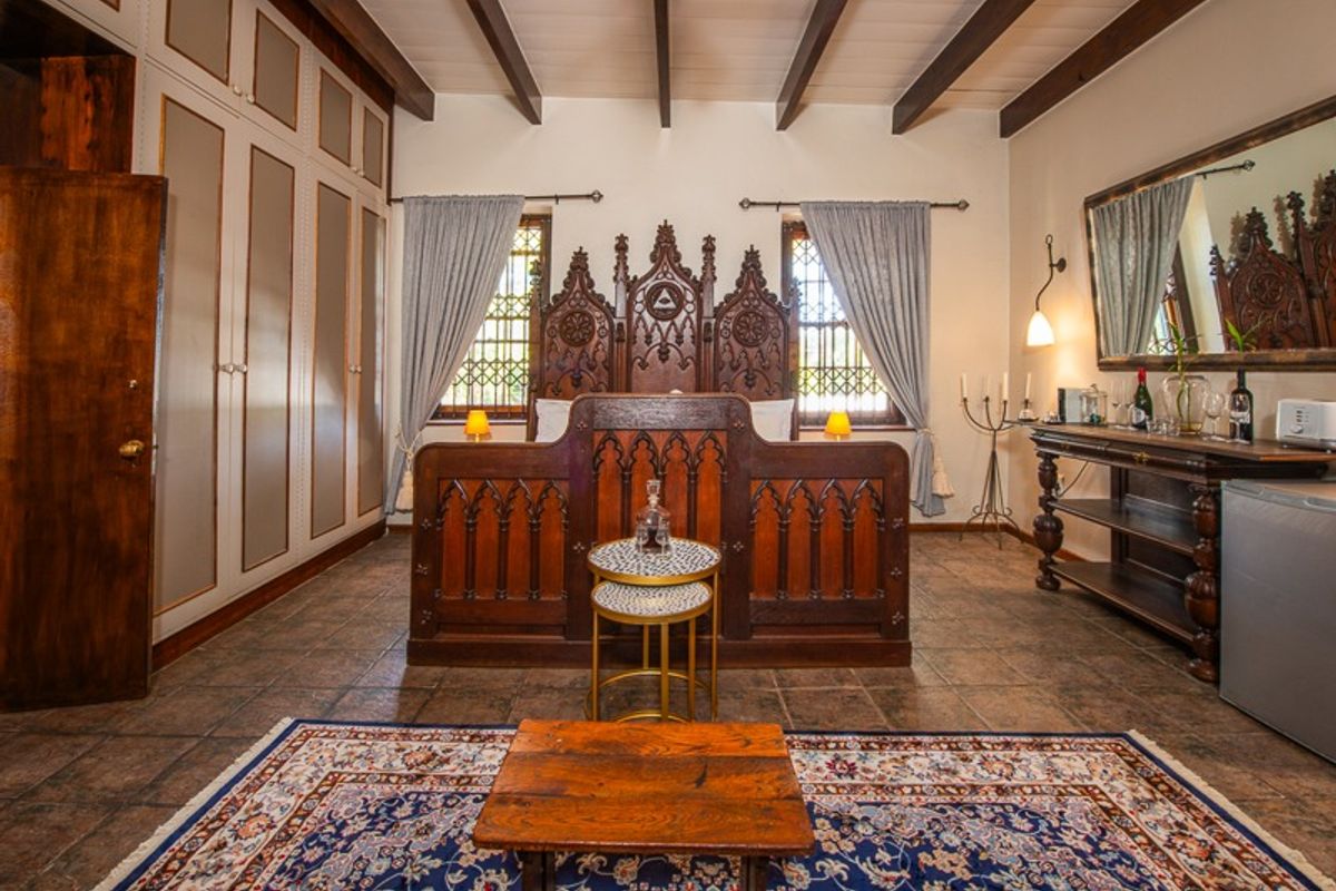A well-maintained bedroom featuring exposed timber ceiling beams, tiled flooring, and custom built-in cabinetry, complemented by decorative leaded glass windows.