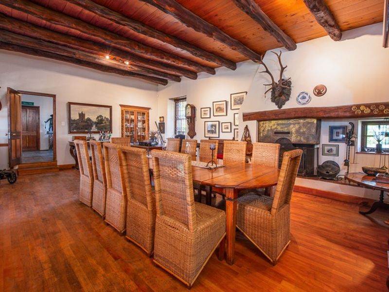 Spacious dining room featuring rustic exposed timber ceiling beams, warm hardwood flooring, and a traditional built-in fireplace with a timber mantelpiece.