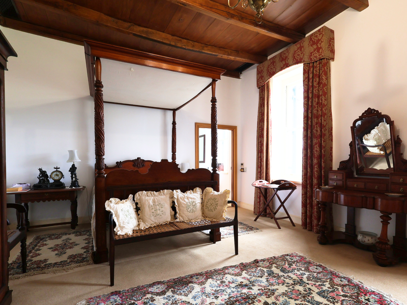A spacious bedroom featuring a high timber-beamed ceiling, neutral carpeting, and a large window allowing for natural light.