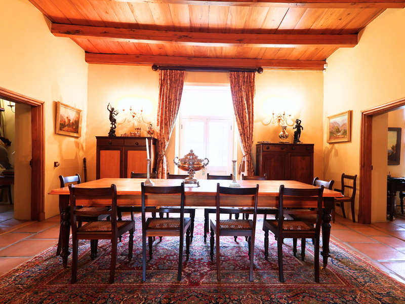 A formal dining room featuring traditional exposed timber ceiling beams, terracotta floor tiles, and classic timber door frames connecting to adjacent living spaces.