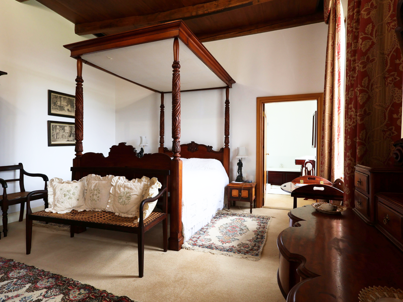 Spacious bedroom featuring exposed timber ceiling beams, neutral carpeting, and direct access to an adjoining bathroom.