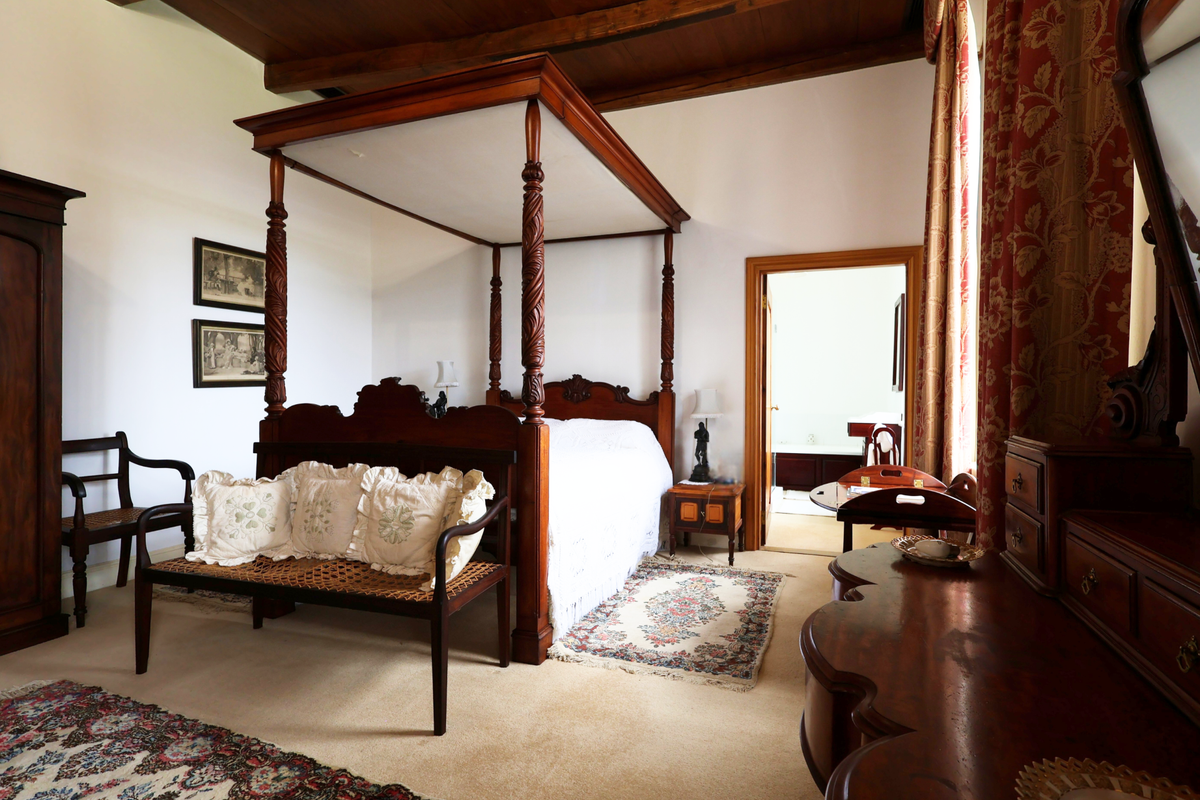Spacious bedroom featuring exposed timber ceiling beams, neutral carpeting, and direct access to an adjoining bathroom.