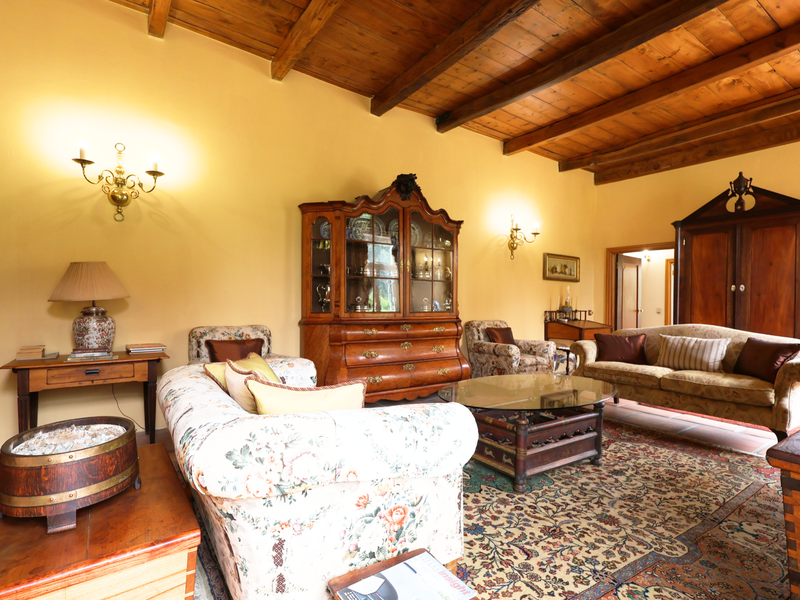 A spacious living room featuring a high exposed timber beam ceiling, warm yellow walls, and traditional terracotta floor tiles.