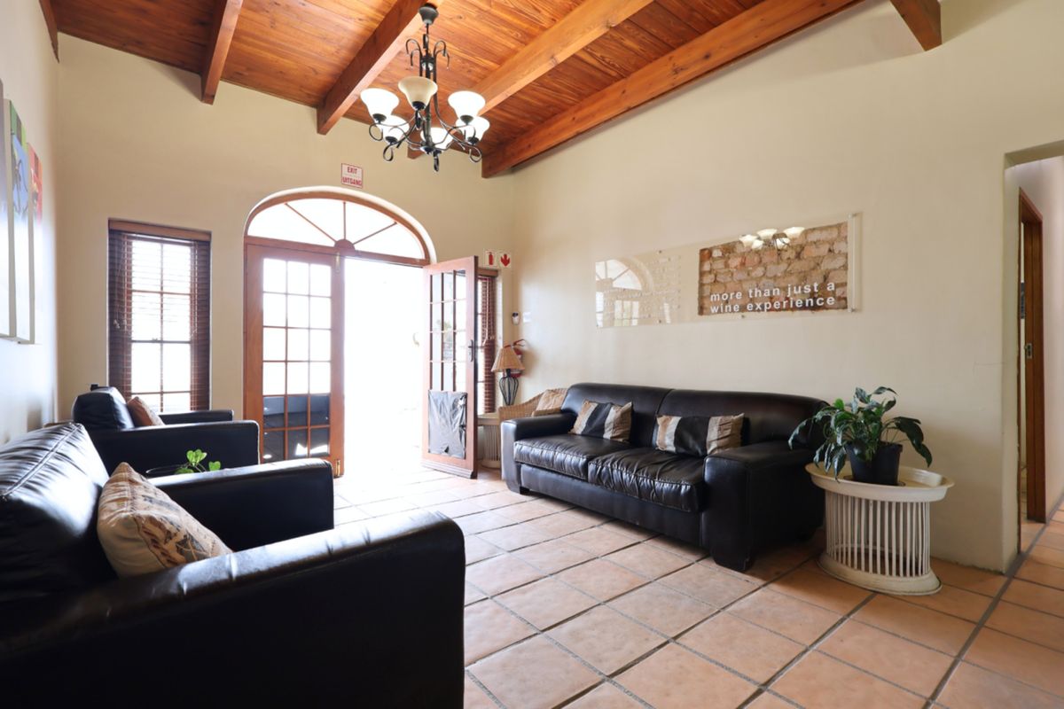 A rustic living area featuring exposed timber beam ceilings, terracotta tiled flooring, and an arched entrance door with natural light.