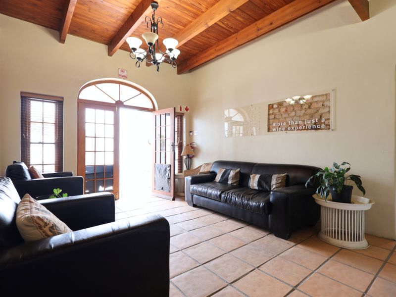 A rustic living area featuring exposed timber beam ceilings, terracotta tiled flooring, and an arched entrance door with natural light.