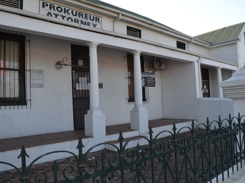Front facade of a professional office building featuring a covered veranda, classical columns, and secure wrought iron fencing.