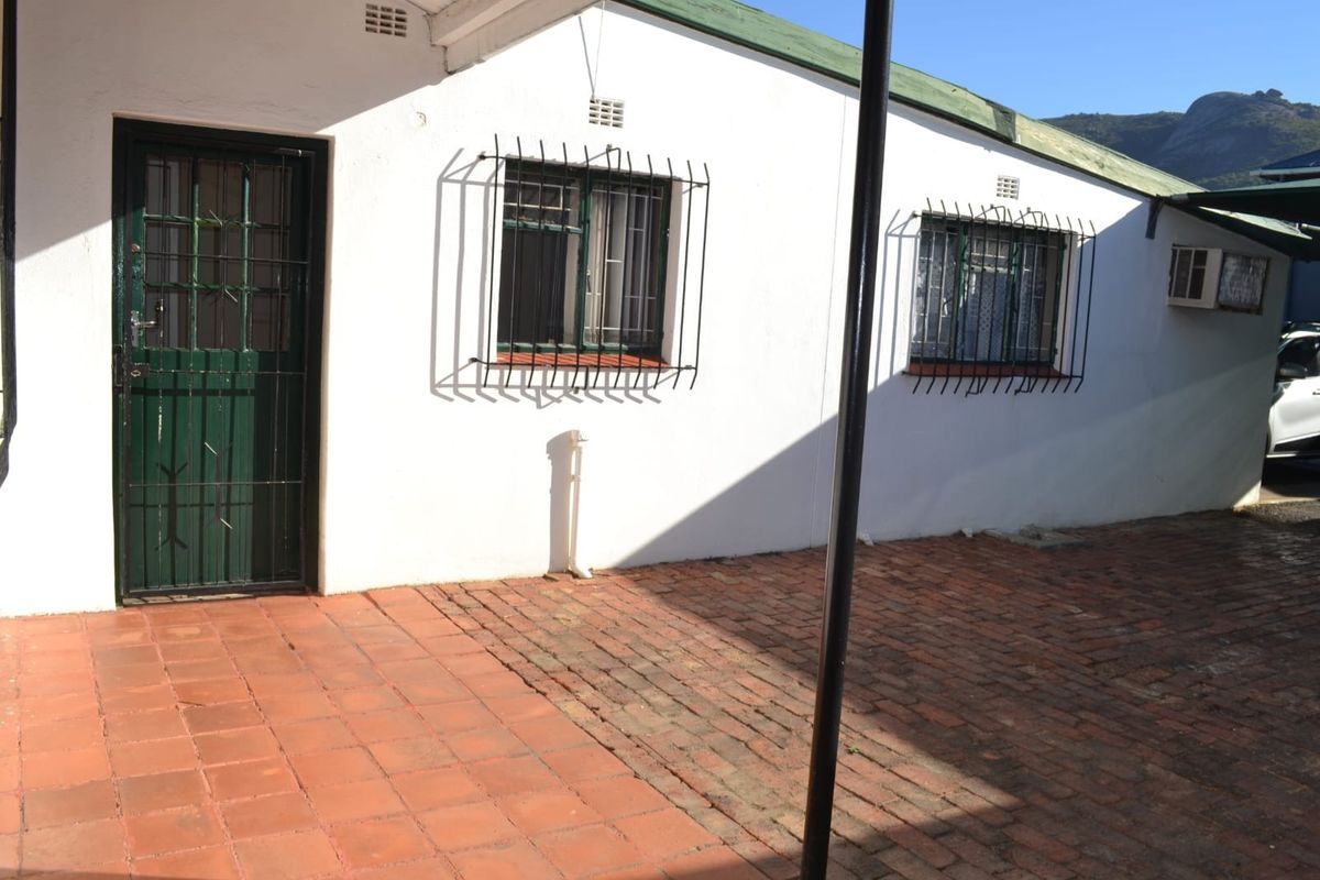 Rear exterior view of the office building featuring brick paving, security bars on windows, and a metal security gate.