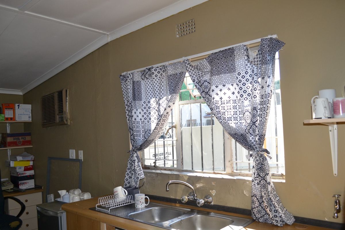 A functional kitchen area featuring a double stainless steel sink, window security bars, and an integrated air conditioning unit.