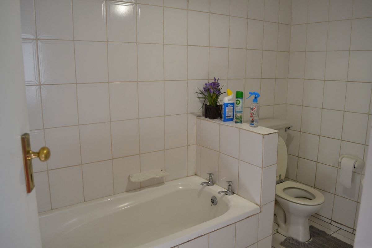 A functional bathroom featuring a bathtub and toilet with full-height wall tiling and a built-in partition wall.