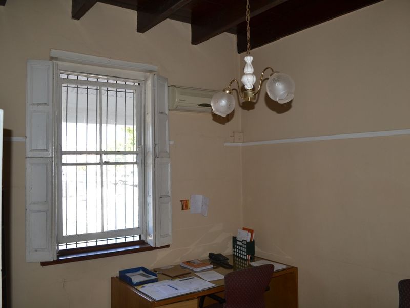 A functional office space featuring exposed timber ceiling beams, security-barred windows with timber shutters, and a wall-mounted air conditioning unit.