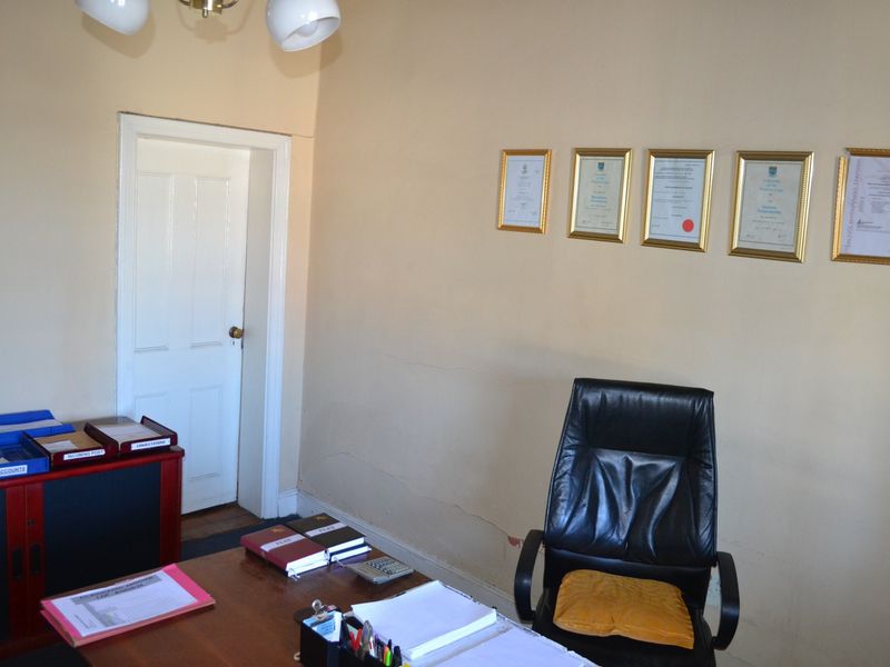 A functional office space featuring neutral walls, a classic panelled door, and visible hairline cracks requiring minor maintenance.