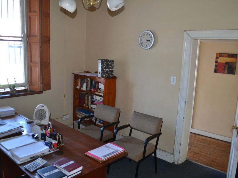 A functional office space featuring timber window shutters, security bars, and neutral wall finishes, suitable for a professional work environment.