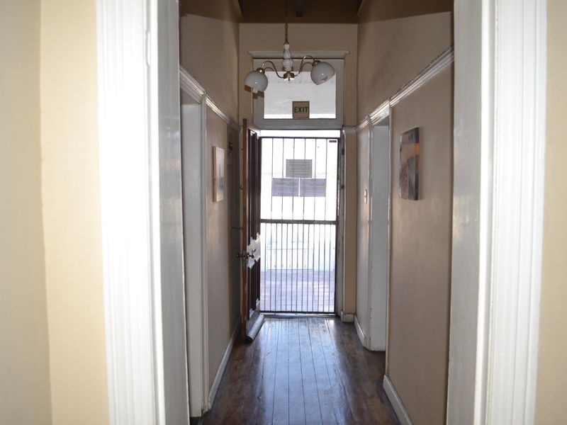 A functional hallway featuring timber flooring, a security gate at the entrance, and traditional architectural details including skirting boards and architraves.