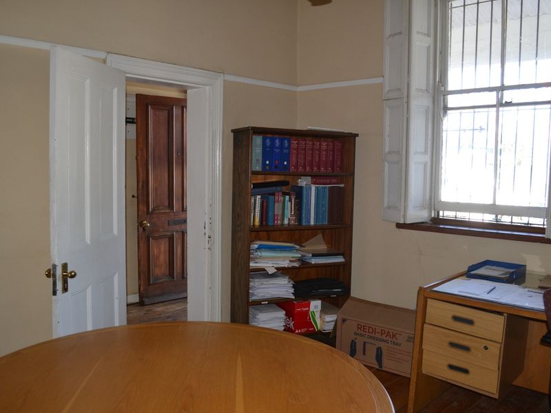 A functional office space featuring traditional timber sash windows with security bars and classic timber door frames, requiring cosmetic updates to finishes.