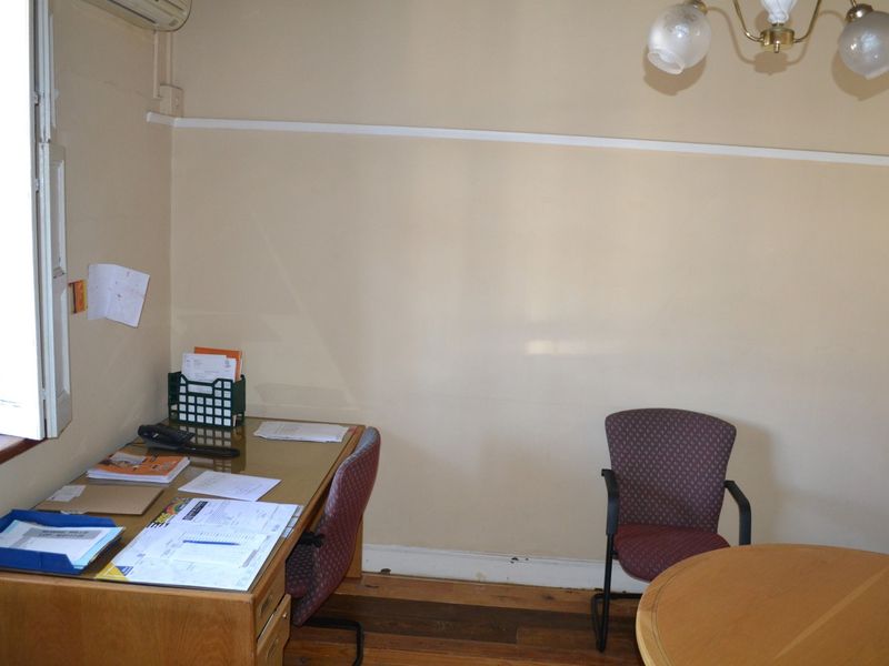 A functional office space featuring hardwood flooring, an air conditioning unit, and natural light from a side window.