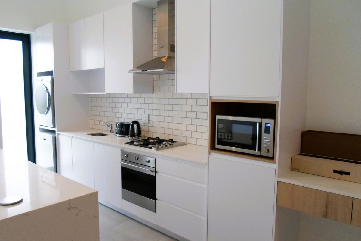Modern kitchen featuring white cabinetry, stone countertops, subway tile backsplash, built-in oven, gas hob, extractor fan, and integrated microwave.