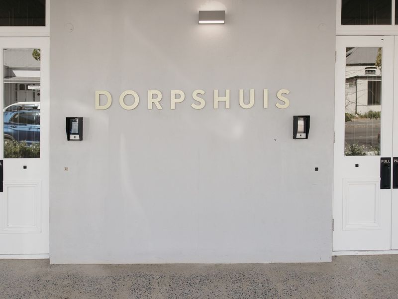 The front entrance of the Dorpshuis apartment building, featuring double doors, intercom access, and modern exterior lighting.