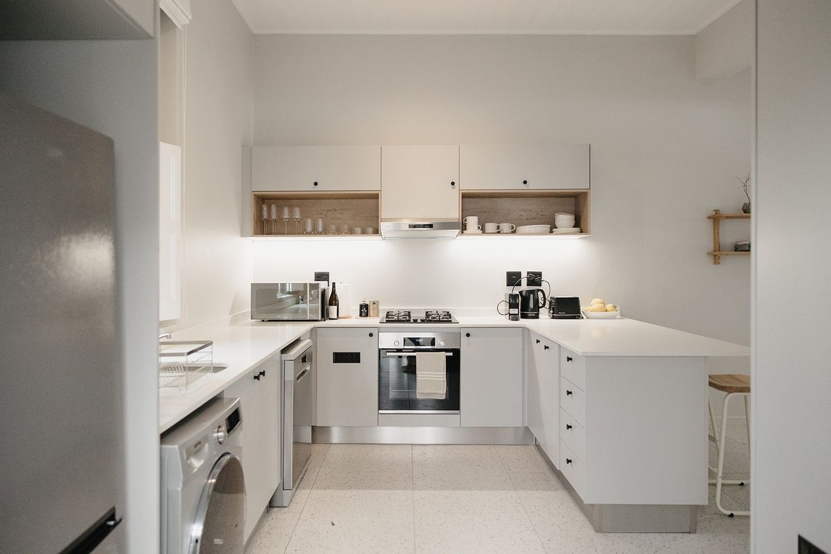 Modern, well-lit kitchen featuring sleek white cabinetry, stone countertops, integrated appliances, and stylish terrazzo flooring, offering a clean and functional culinary space.