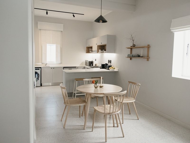 Modern open-plan kitchen and dining area featuring sleek cabinetry, integrated appliances, terrazzo flooring, and contemporary lighting fixtures in a bright, minimalist space.