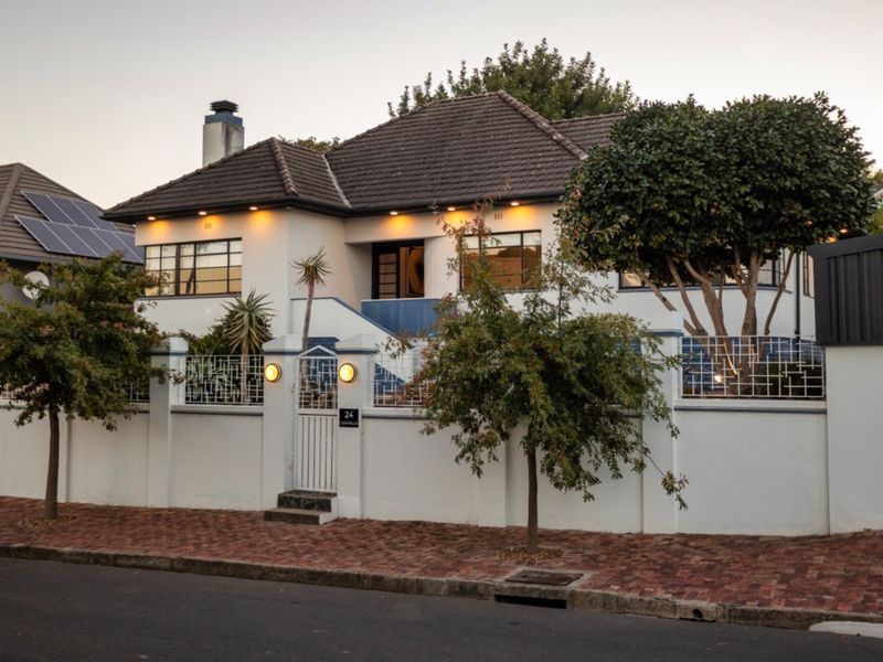 A well-maintained front elevation of a house featuring a tiled roof, secure perimeter wall with pedestrian gate, and integrated exterior lighting.
