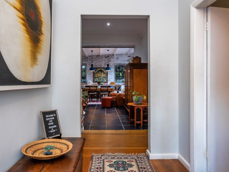 A view from the hallway looking through a doorway into an open-plan living and dining area featuring exposed brick walls and mixed flooring.