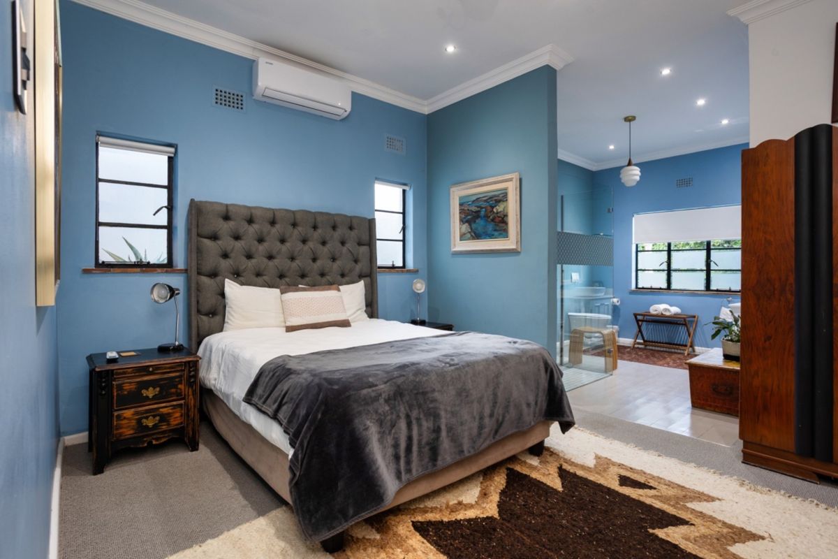 A well-maintained bedroom featuring blue walls, crown molding, recessed lighting, and an integrated en-suite bathroom with a glass shower partition.