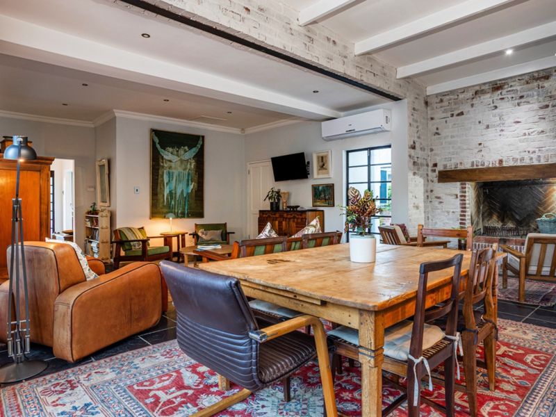 Spacious open-plan living and dining area featuring exposed brick walls, timber ceiling beams, stone flooring, and a traditional wood-burning fireplace.