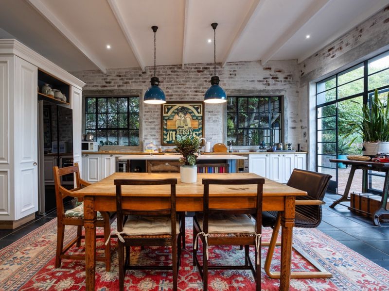 Spacious open-plan kitchen and dining area featuring exposed brick walls, industrial-style steel windows, stone flooring, and high-quality built-in cabinetry with a central island.