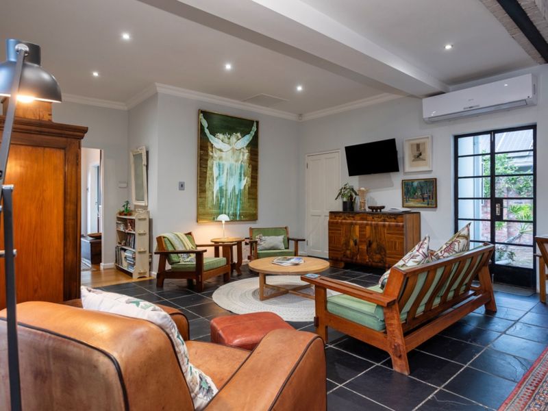 A well-maintained living room featuring stone tile flooring, recessed downlighting, an exposed ceiling beam, and a split-system air conditioner with access to the outdoors.