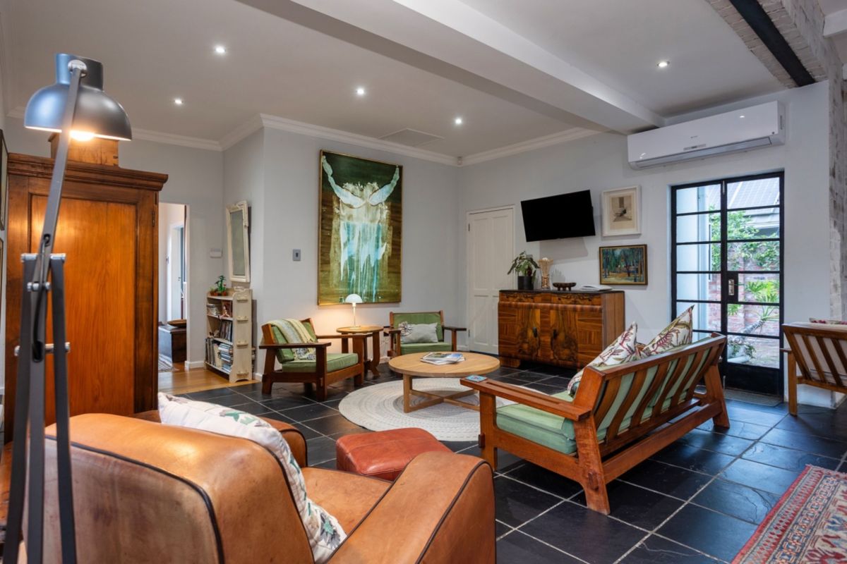 A well-maintained living room featuring stone tile flooring, recessed downlighting, an exposed ceiling beam, and a split-system air conditioner with access to the outdoors.