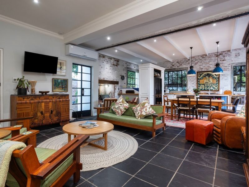 Spacious open-plan living and dining area featuring exposed brick walls, slate flooring, exposed ceiling beams, and modern recessed lighting.