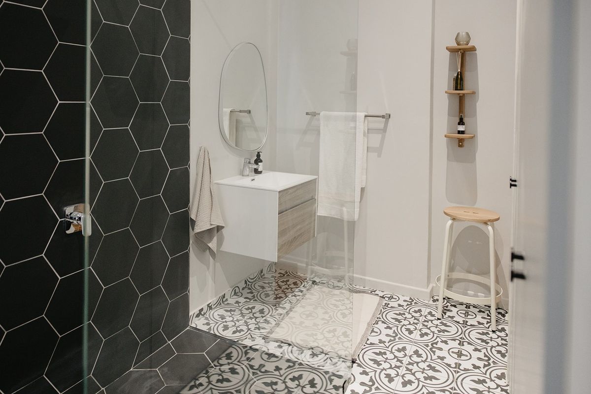 Modern bathroom featuring a wall-mounted vanity, striking hexagonal feature wall tiles, patterned floor tiling, and a glass-enclosed shower area.