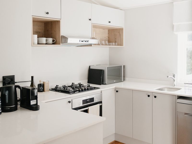 Modern kitchen featuring white cabinetry, stone countertops, gas cooktop, built-in oven, and integrated sink with a clean, minimalist aesthetic.