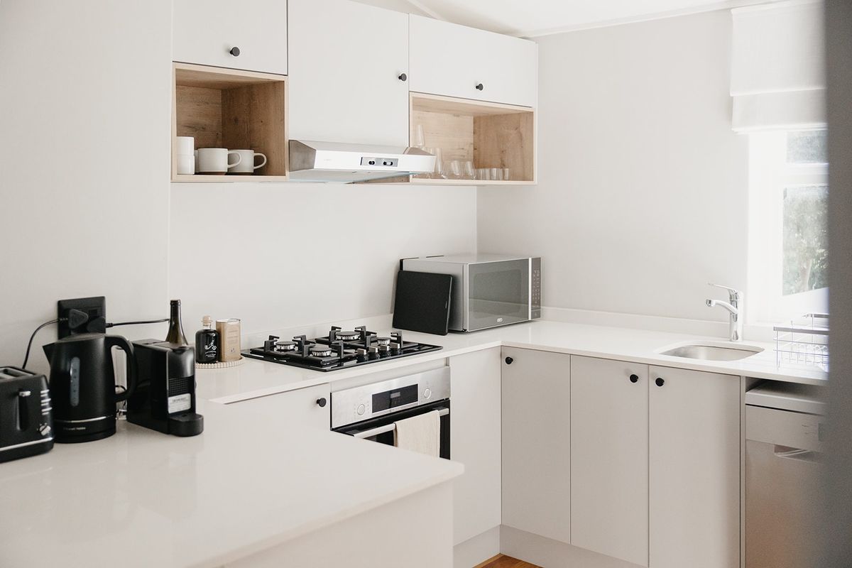 Modern kitchen featuring white cabinetry, stone countertops, gas cooktop, built-in oven, and integrated sink with a clean, minimalist aesthetic.