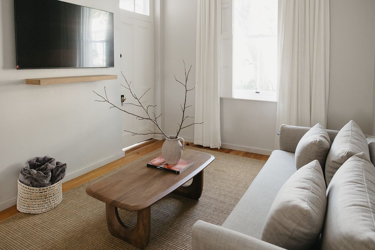Bright and inviting living room featuring polished hardwood flooring, a minimalist timber floating shelf, and a classic panelled entrance door.