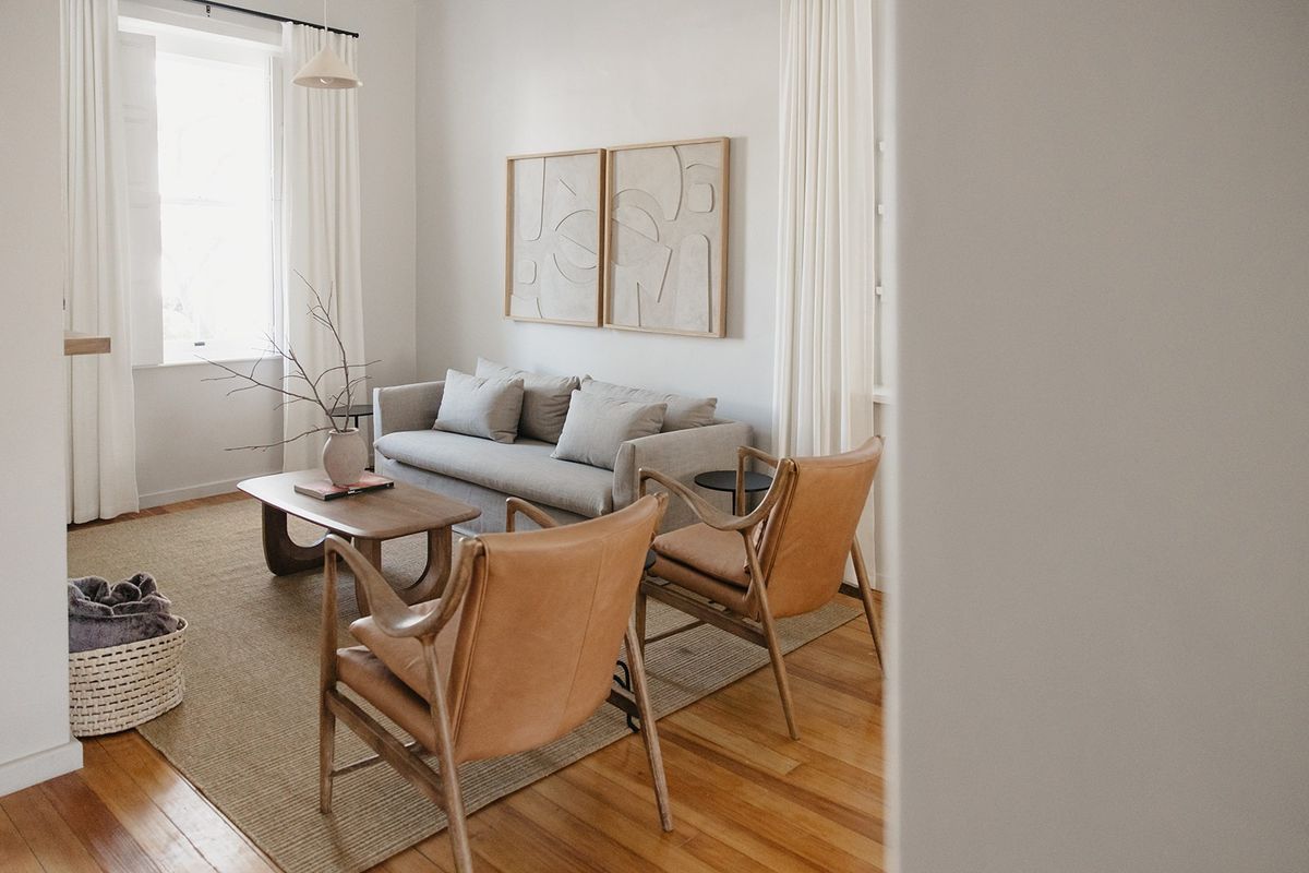 A bright and well-maintained living room featuring polished hardwood flooring and large sash windows with elegant curtain treatments.